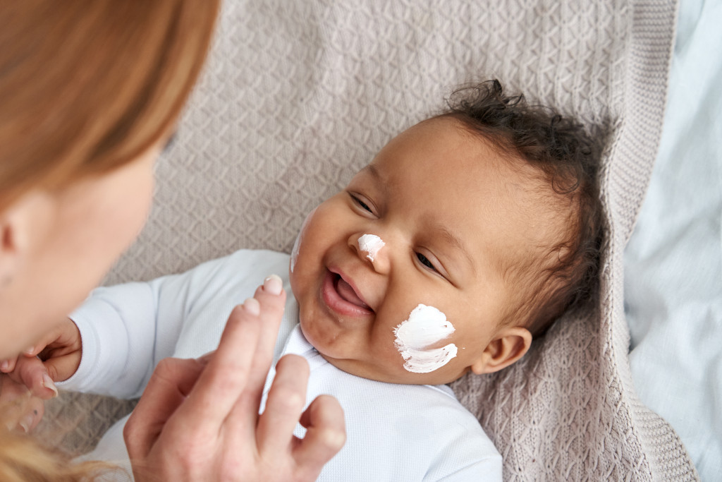 a baby with moisturizer on the face applied by mother