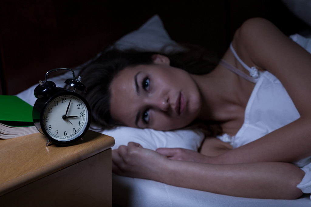 a woman with insomnia lying in bed awake and looking at an alarm clock