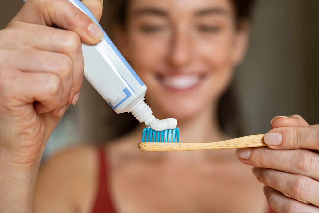 a woman smiling as she's putting toothpaste on her toothbrush