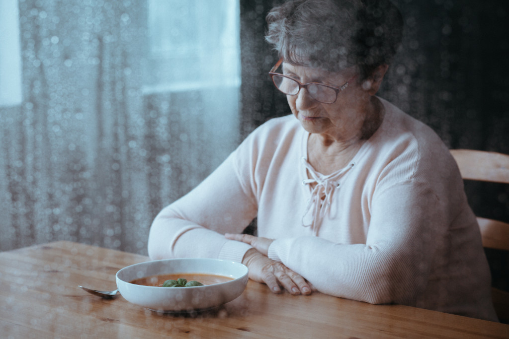 A sad senior woman looking at her food