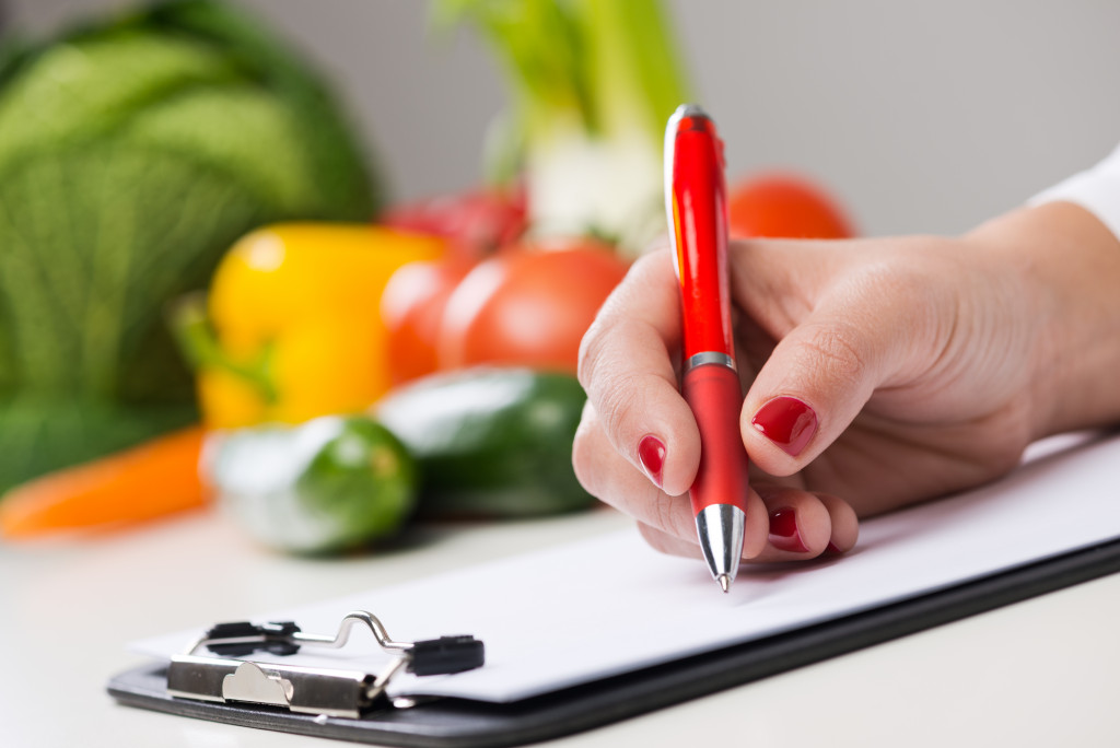 A nutritionist writing on medical records with vegetables in the background