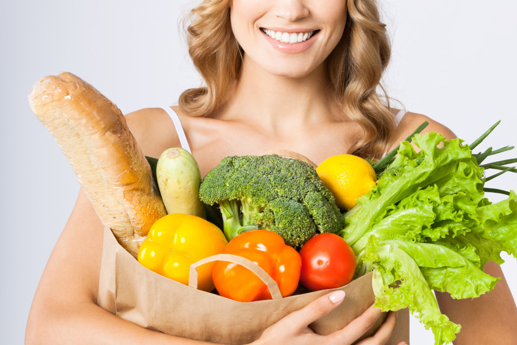 a woman holding a bag of groceries filled with vegetables and fruits