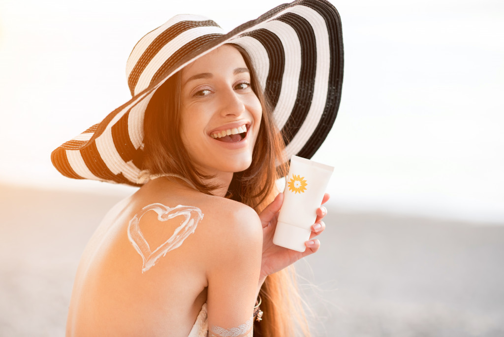 a woman with a hat and a heart shaped lotion on her shoulder smiling