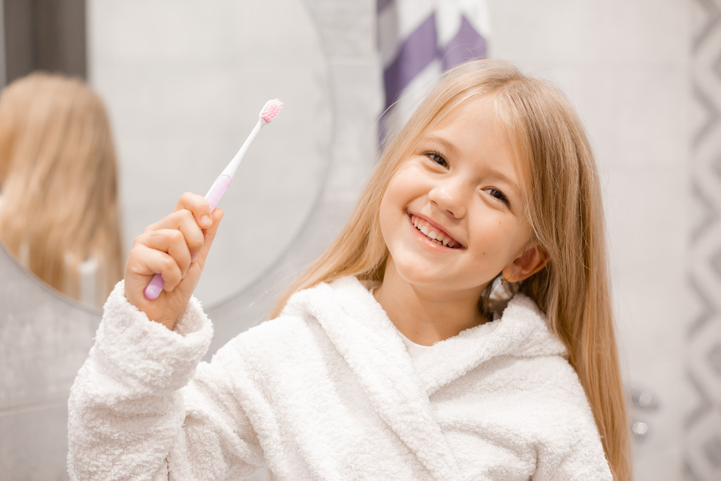 A child holding a toothbrush while smiling to the camera