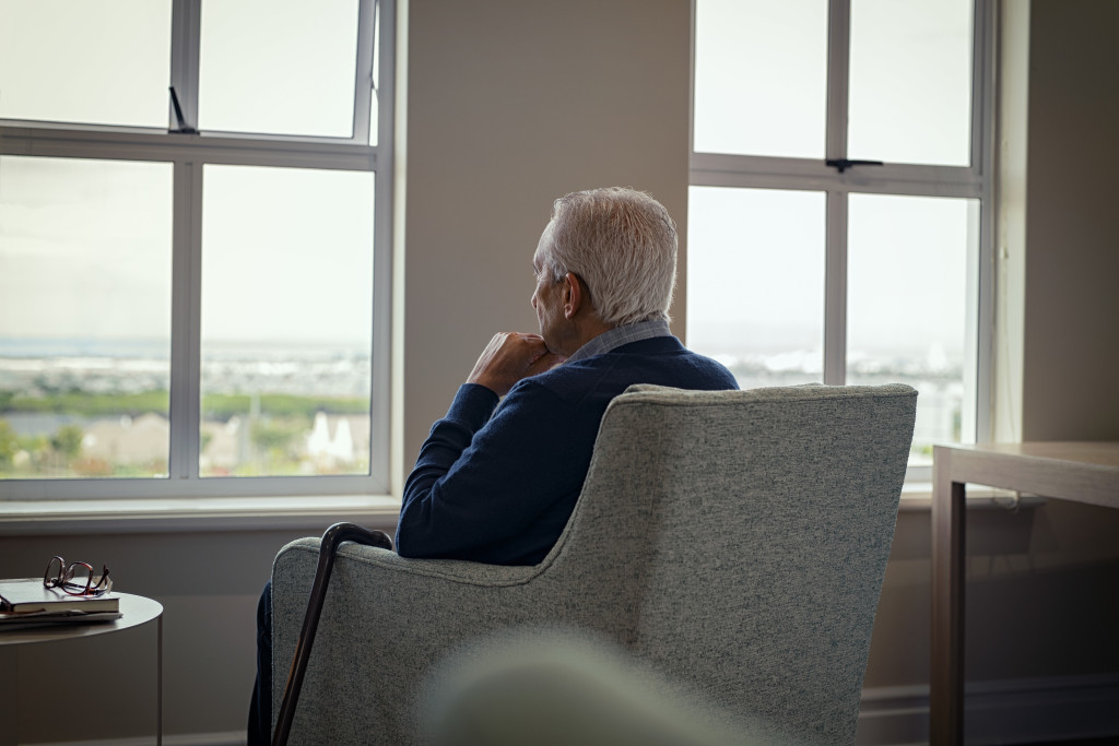 sad elderly man looking out at the window with gloomy weather