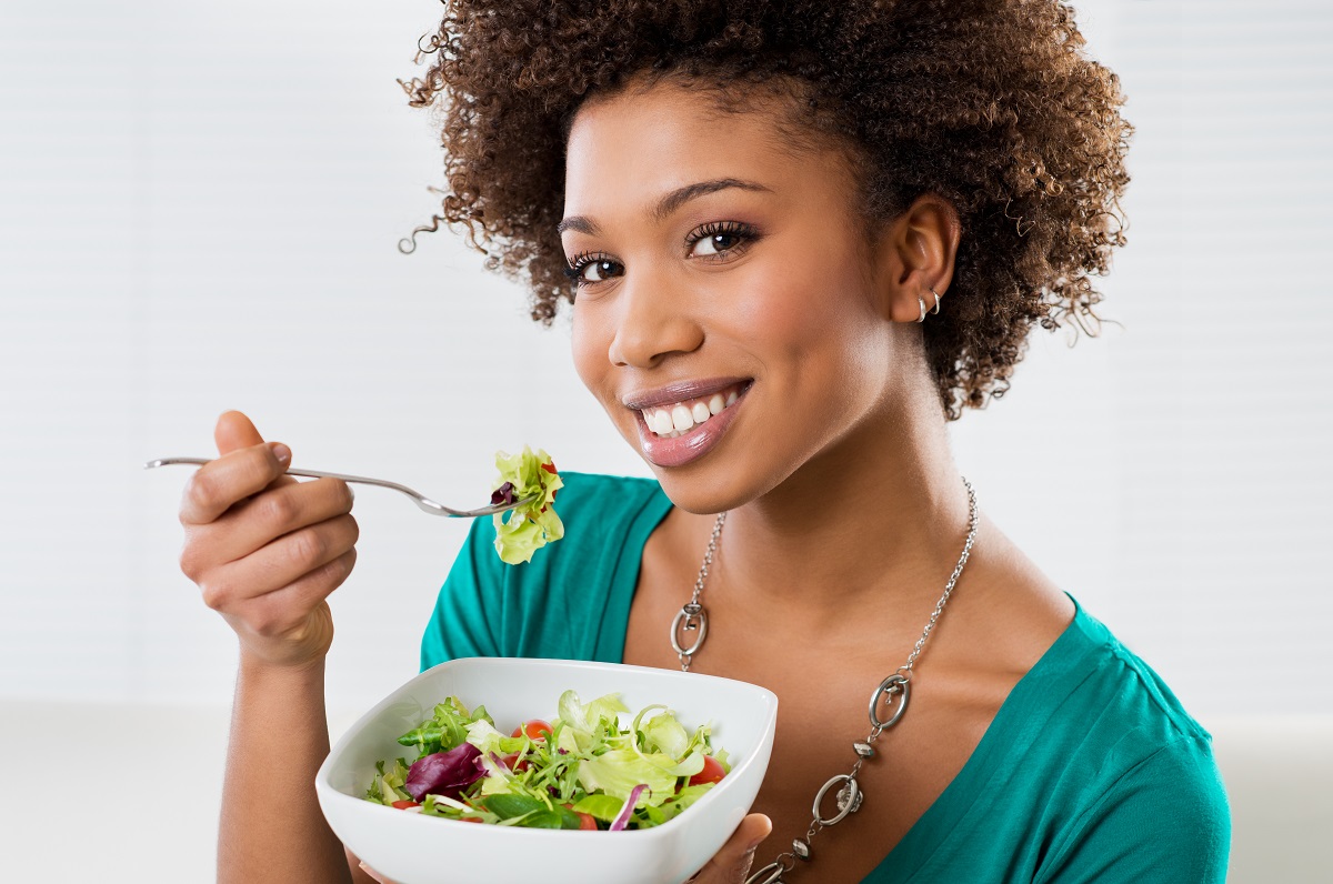 Young woman smiling while eating a salad.